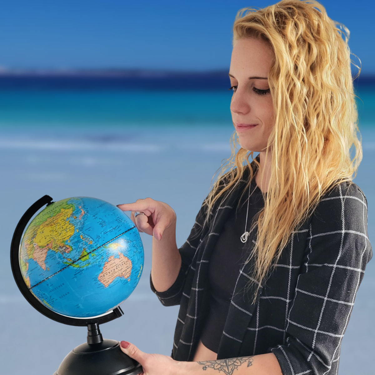 Julia von Hadscho Unterwegs zeigt auf einen Globus am Strand und bietet persönliche Reiseberatung und individuelle Reiseplanung weltweit