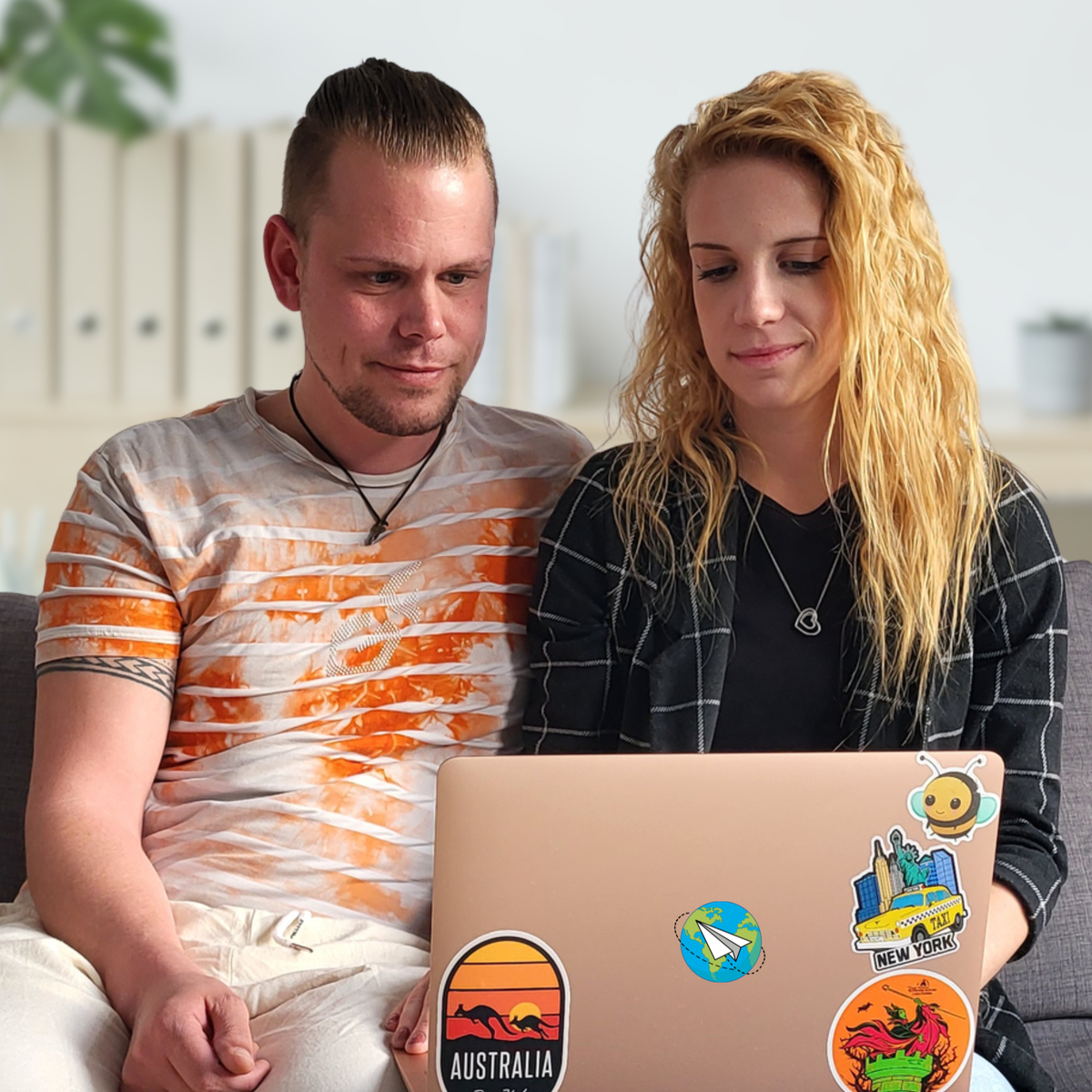 Olli und Julia von Hadscho Unterwegs sitzen gemeinsam vor einem Laptop mit Reise-Stickern und planen eine Reise, persönliche Reiseberatung weltweit